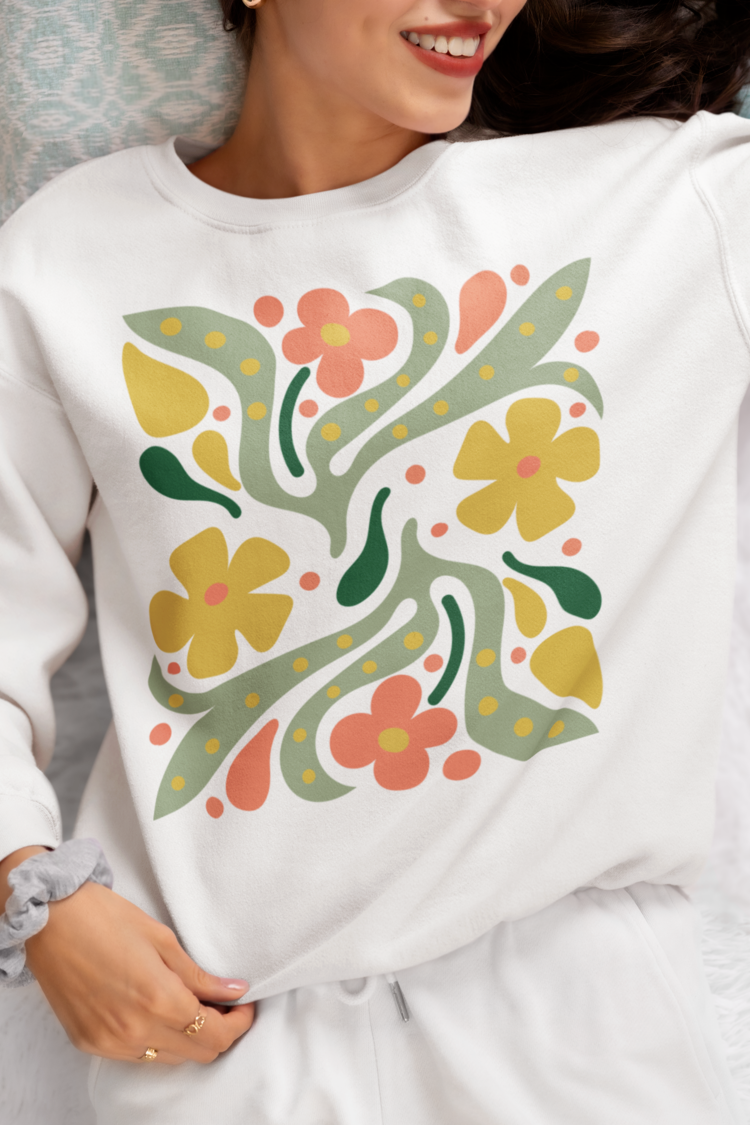 A close-up of a person wearing a white crewneck sweatshirt with a retro floral pattern in yellow, orange, and green, paired with white sweatpants.