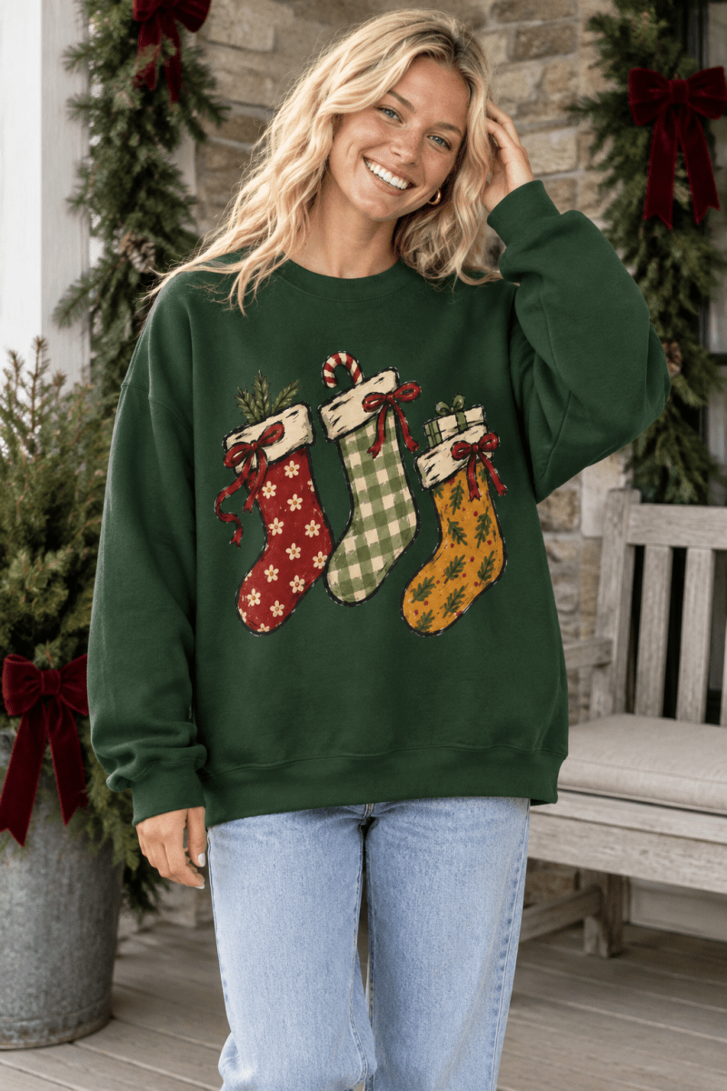 Woman wearing a dark green The Doodled Flower Boutique crewneck sweatshirt featuring hand-drawn Christmas stockings.