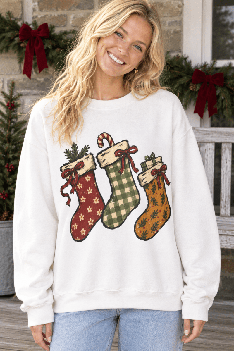 A woman wearing a The Doodled Flower Boutique cream crewneck sweatshirt featuring hand-drawn Christmas stockings.