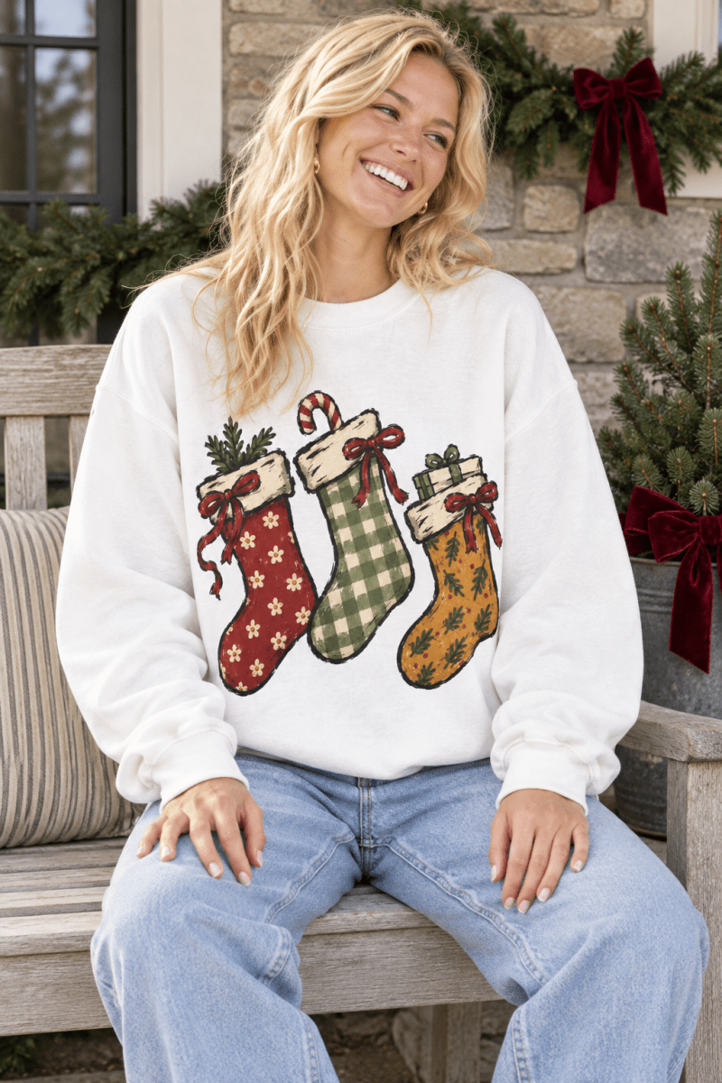 The Doodled Flower Boutique white crewneck sweatshirt featuring hand-drawn Christmas stockings with festive patterns.