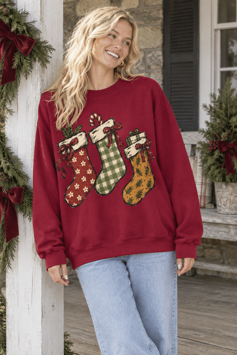 Woman wearing a The Doodled Flower Boutique cranberry red crewneck sweatshirt with hand-drawn Christmas stocking art.