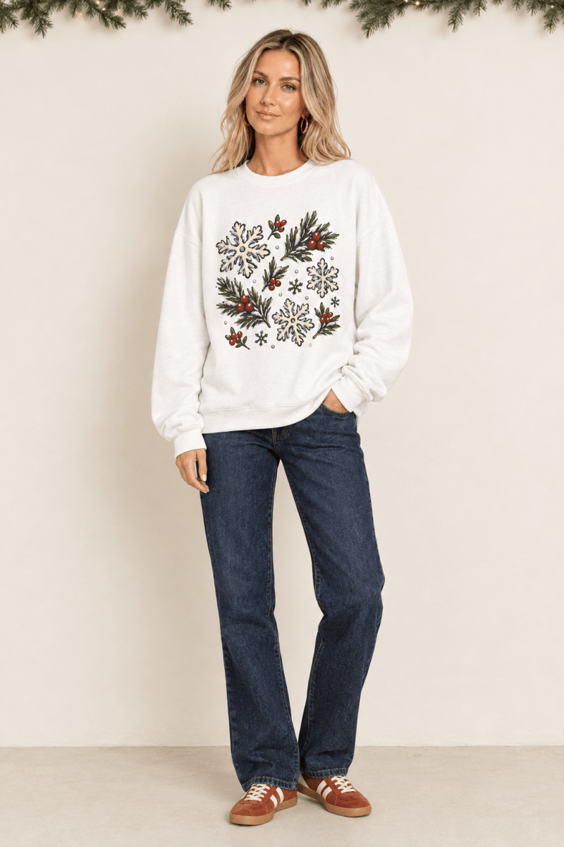 The Doodled Flower Boutique white crewneck sweatshirt with hand-drawn snowflake, evergreen, and berry holiday print.