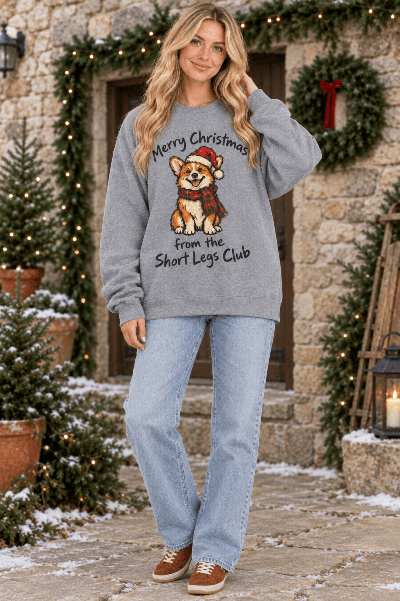 Woman wearing a The Doodled Flower Boutique graphite heather Christmas sweatshirt with a corgi illustration outdoors.