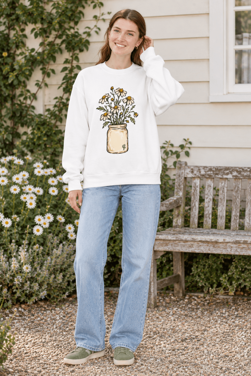 Woman wearing The Doodled Flower Boutique cream crewneck sweatshirt with a daisy bouquet illustration in a jar.