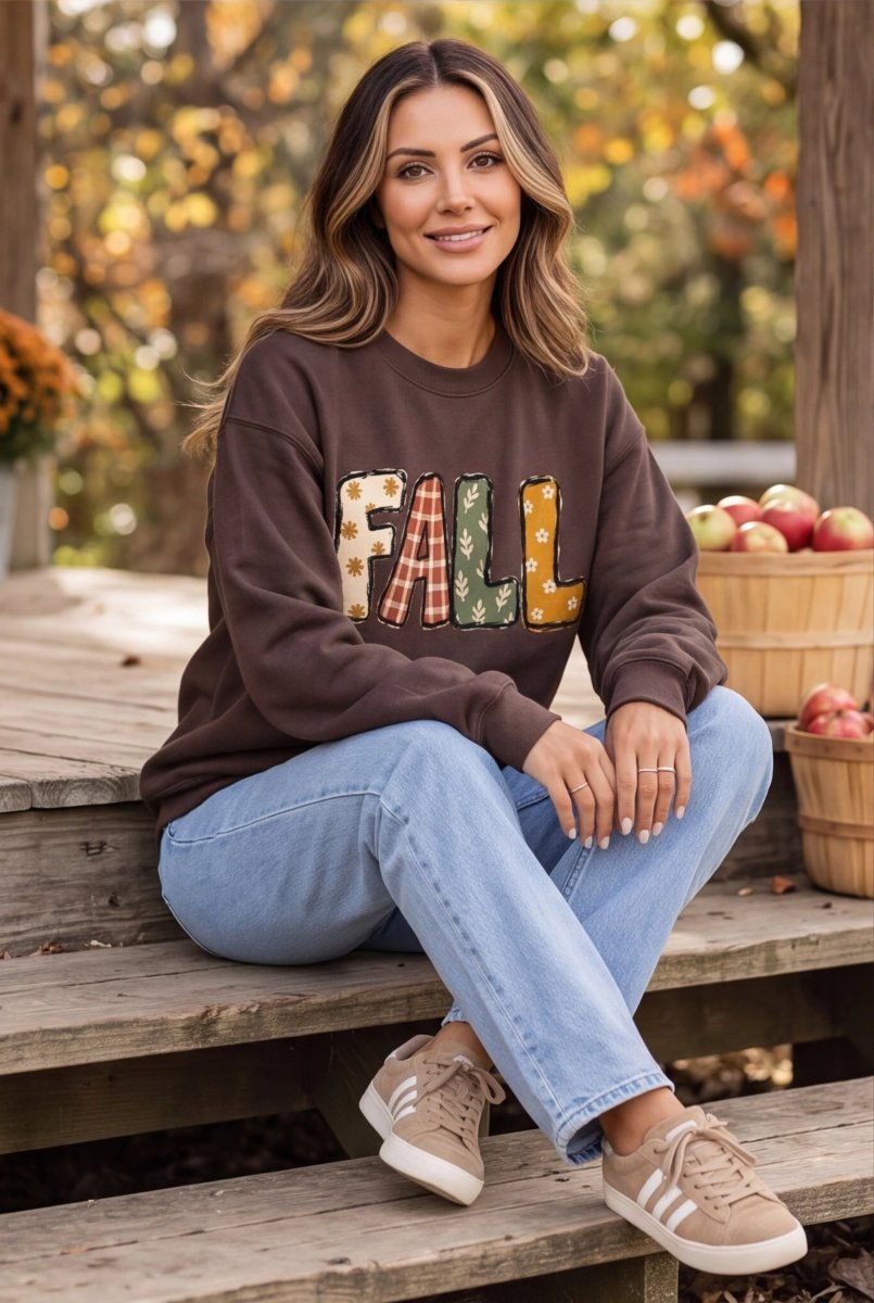 The Doodled Flower Boutique espresso brown crewneck sweatshirt with patchwork FALL graphic, worn by a smiling woman.