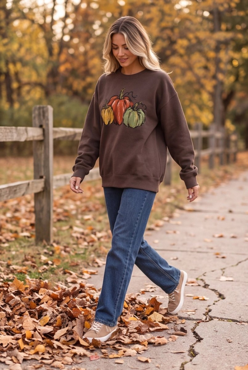 The Doodled Flower Boutique espresso brown cotton sweatshirt with watercolor pumpkin print worn by a woman outdoors.