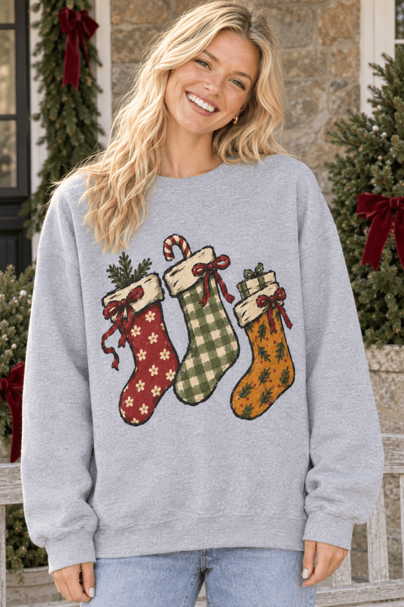 Woman wearing The Doodled Flower Boutique grey crewneck sweatshirt with hand-drawn Christmas stocking illustrations.