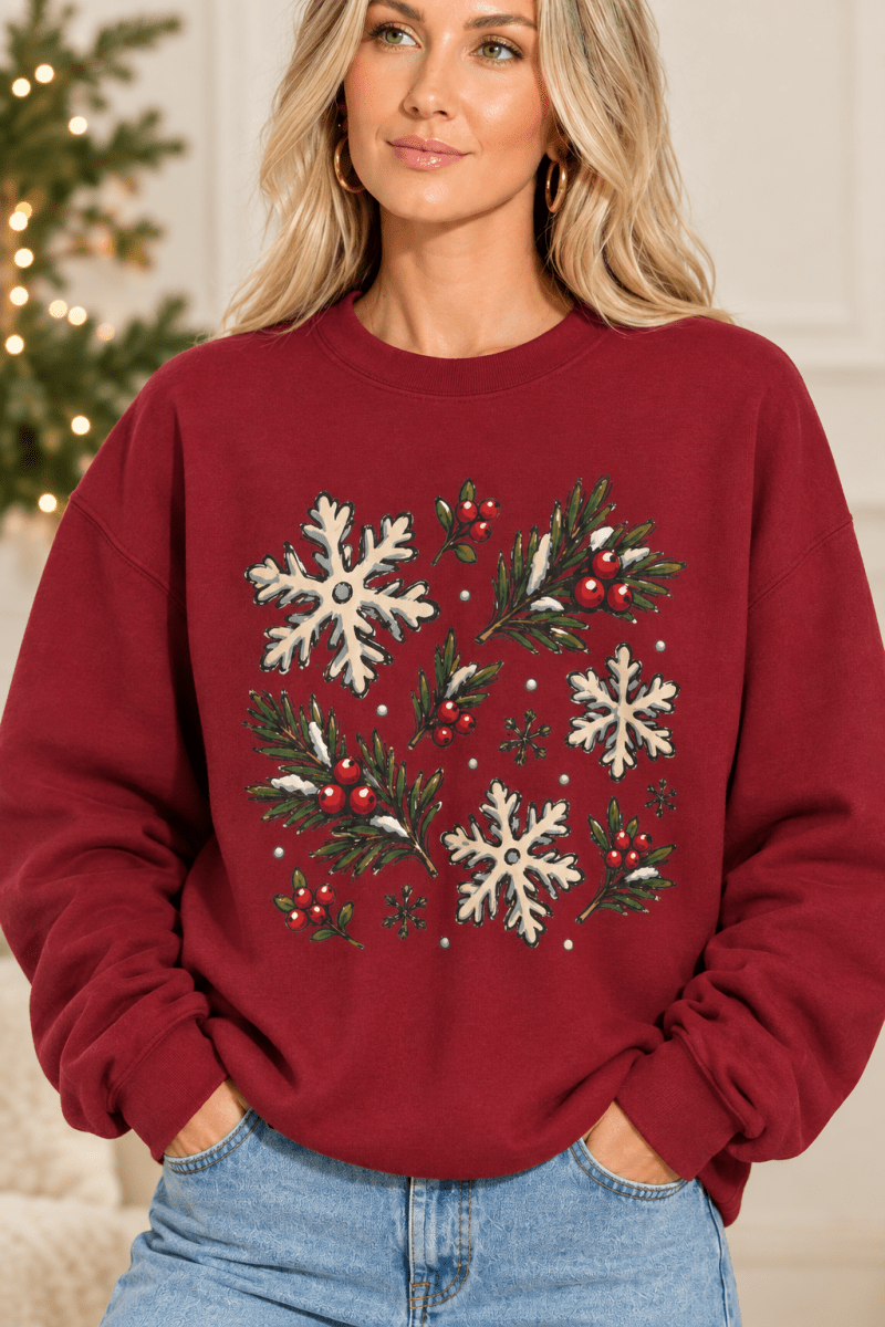 The Doodled Flower Boutique maroon crewneck sweatshirt featuring a hand-drawn print of snowflakes, pine, and berries.