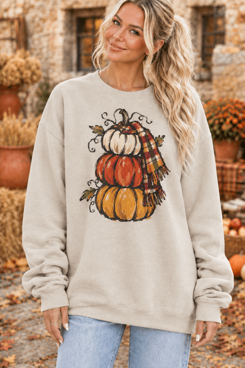 The Doodled Flower Boutique cream crewneck sweatshirt featuring a hand-drawn stacked pumpkin and plaid scarf design.