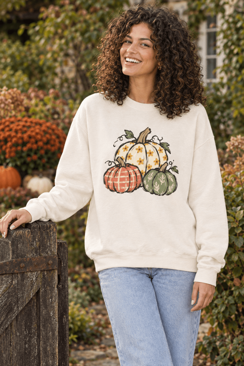 The Doodled Flower Boutique ivory crewneck sweatshirt featuring a hand-drawn pumpkin trio in orange, cream, and sage.