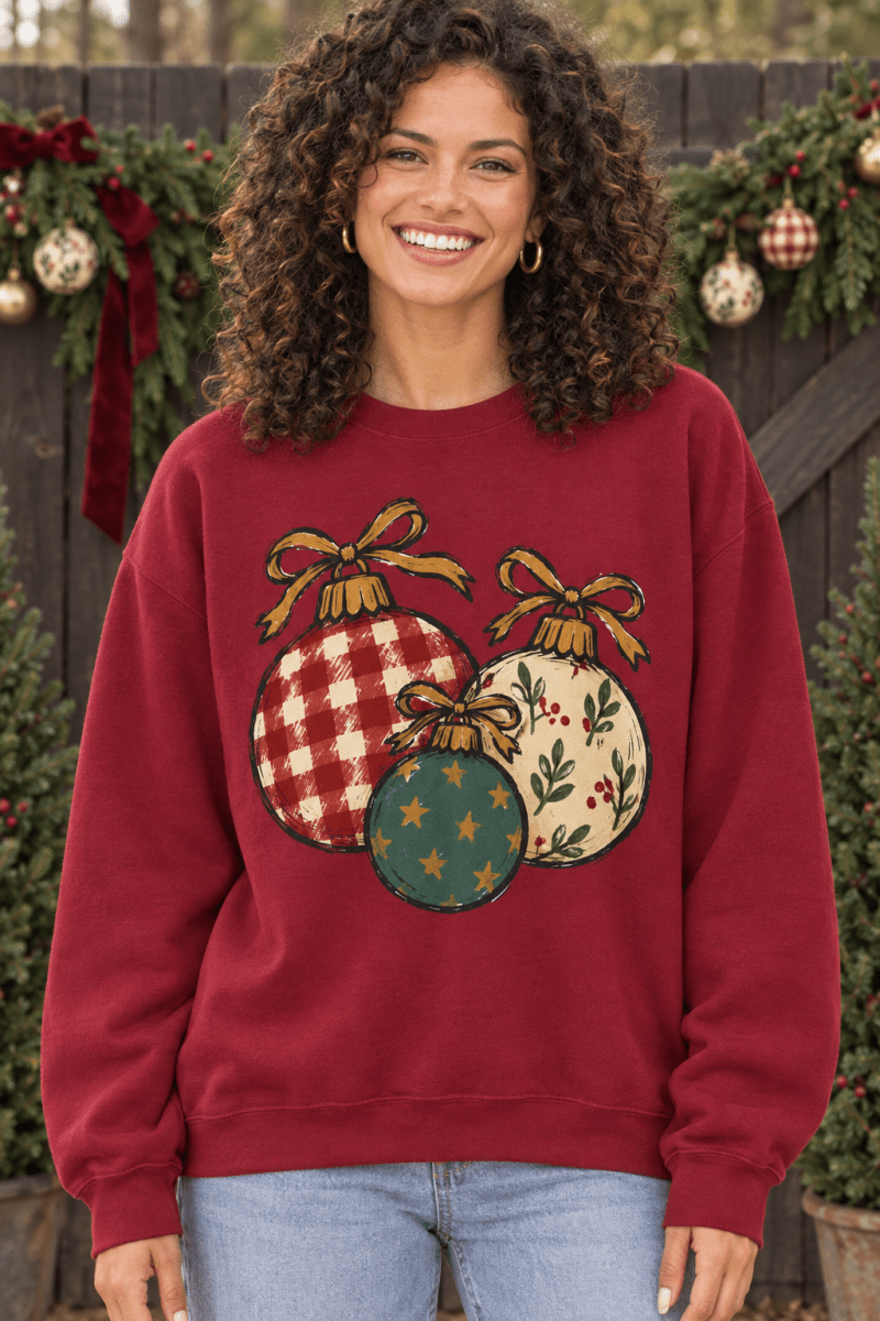Woman wearing a The Doodled Flower Boutique red crewneck sweatshirt with hand-drawn Christmas ornament illustrations.