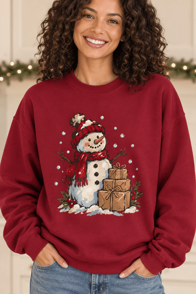 The Doodled Flower Boutique red crewneck sweatshirt featuring a hand-drawn snowman with gifts and falling snow