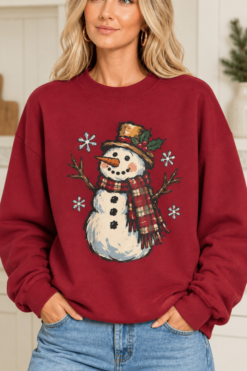 Woman wearing a red The Doodled Flower Boutique crewneck sweatshirt featuring a vintage snowman with a plaid scarf.