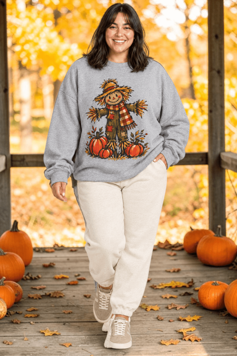The Doodled Flower Boutique grey crewneck sweatshirt featuring a hand-drawn scarecrow and pumpkin harvest graphic.