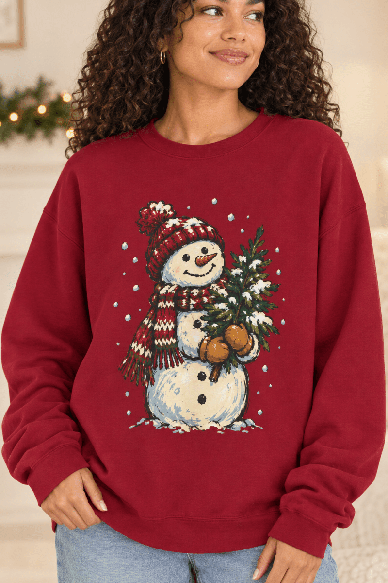 The Doodled Flower Boutique red crewneck sweatshirt featuring a hand-drawn snowman holding a Christmas tree.