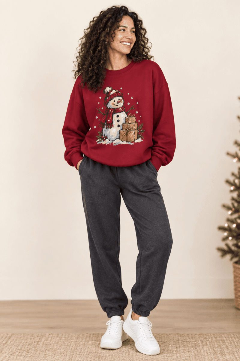 The Doodled Flower Boutique red crewneck sweatshirt featuring a hand-drawn snowman and gift illustration.