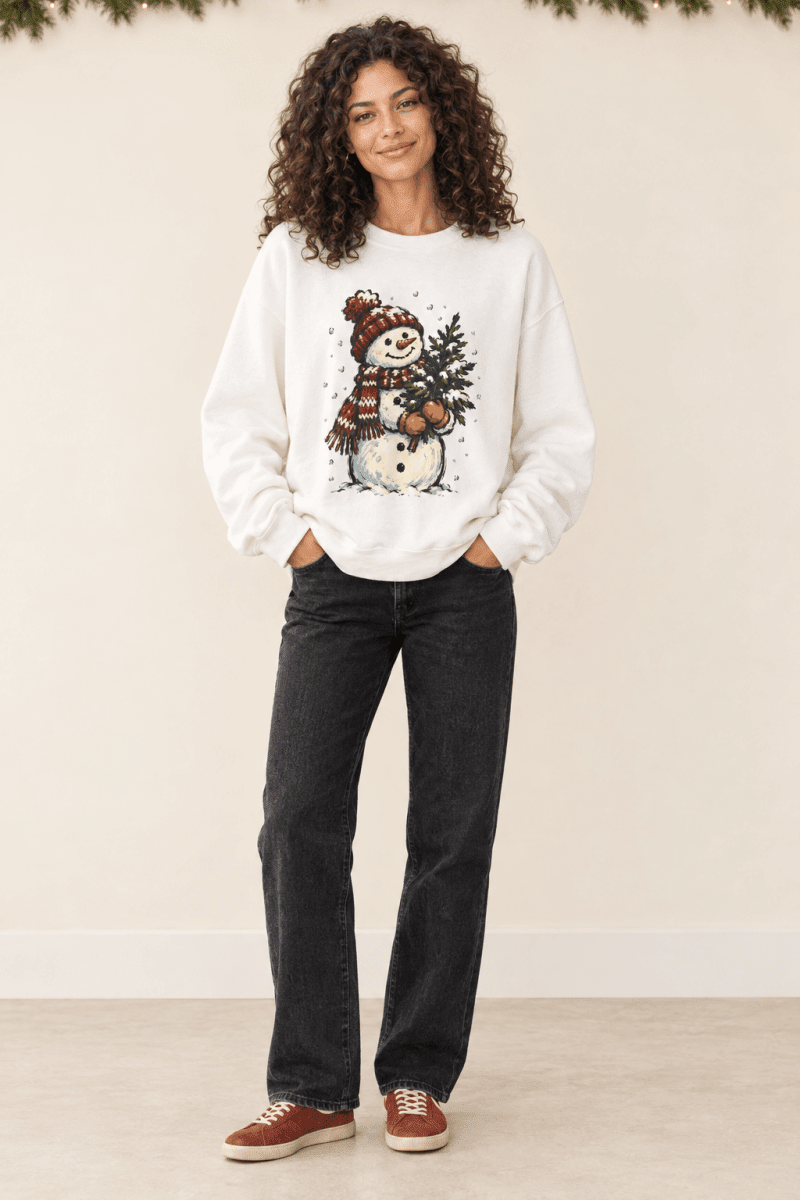 The Doodled Flower Boutique white crewneck sweatshirt featuring a hand-drawn snowman graphic with a Christmas tree.