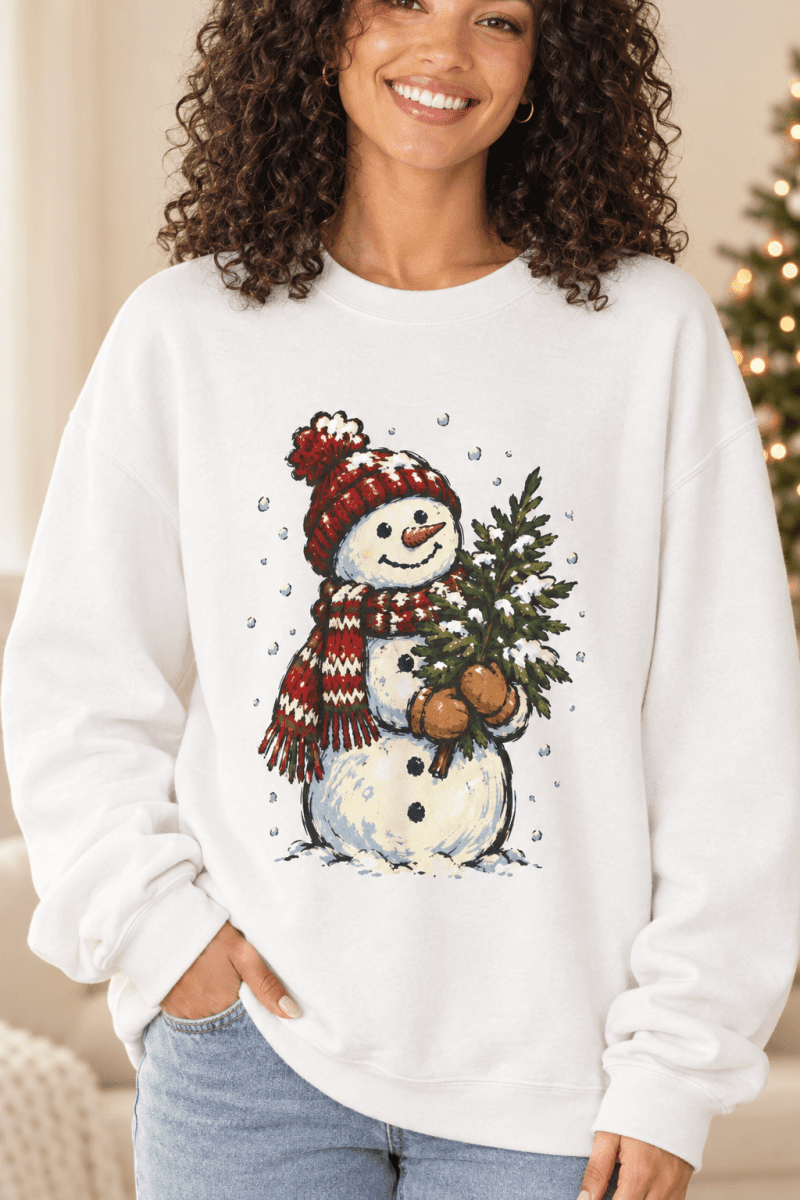 The Doodled Flower Boutique white crewneck sweatshirt featuring a hand-drawn snowman holding a Christmas tree.