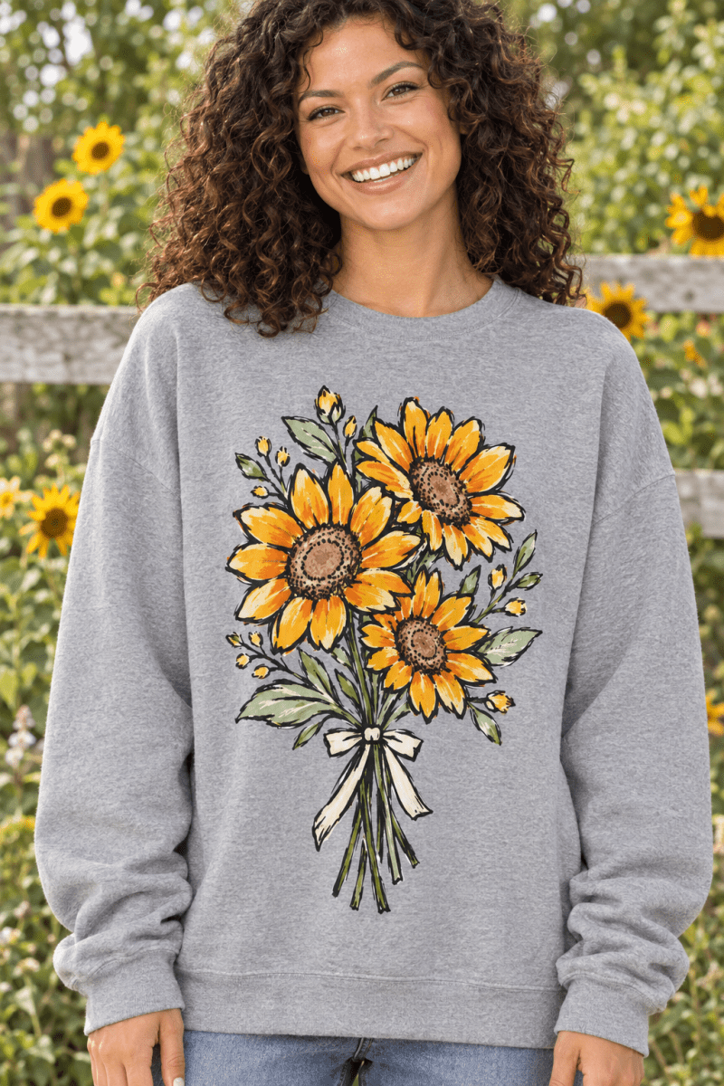 A woman wearing a The Doodled Flower Boutique grey fleece sweatshirt with a hand-drawn sunflower bouquet graphic.
