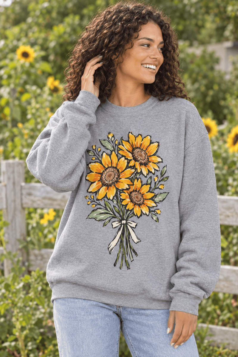 The Doodled Flower Boutique grey fleece sweatshirt with a hand-drawn sunflower bouquet print worn by a smiling woman.