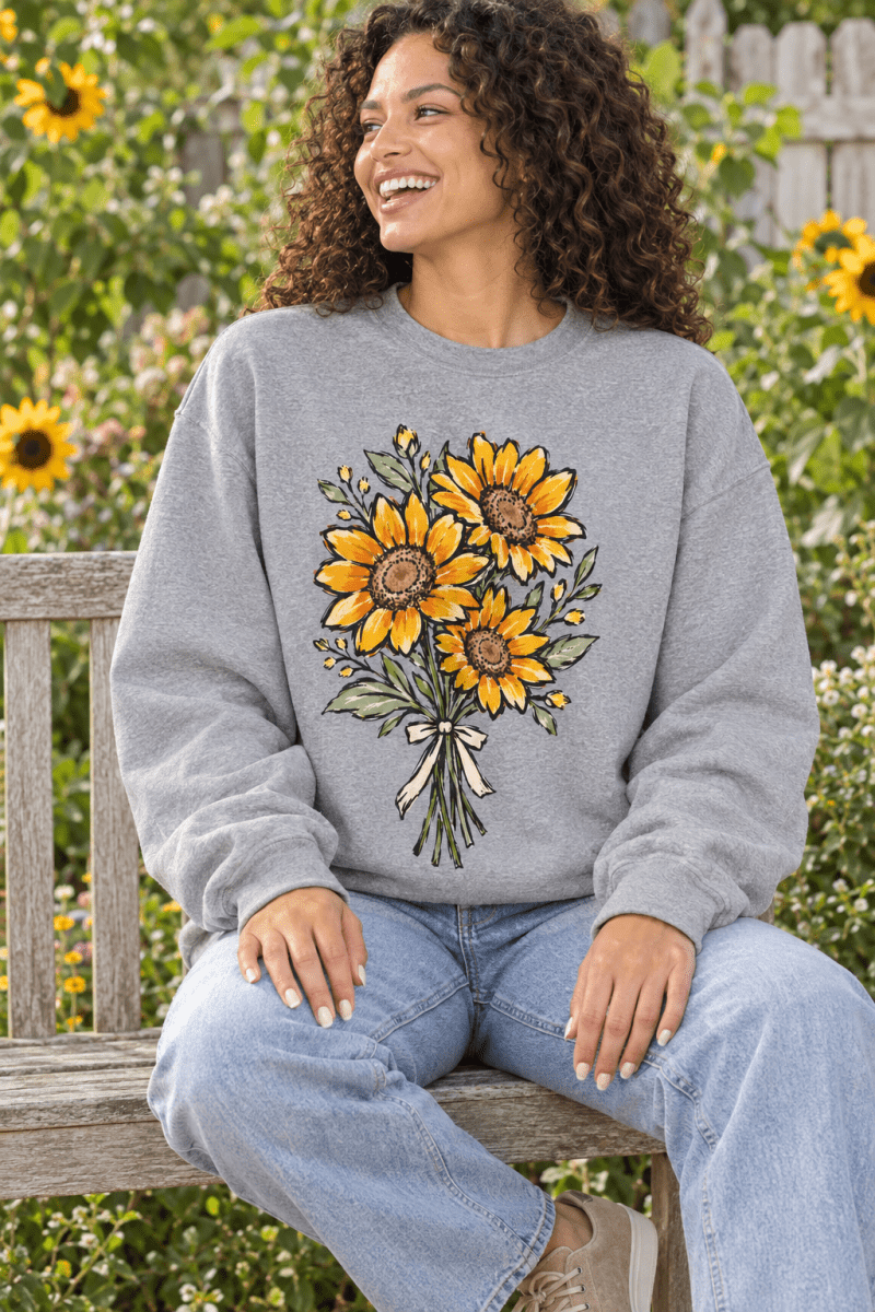 Model wearing The Doodled Flower Boutique grey crewneck sweatshirt with a hand-drawn sunflower bouquet illustration.